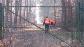 Jagdhelfer in Warnwesten hinter Absperrzaun
