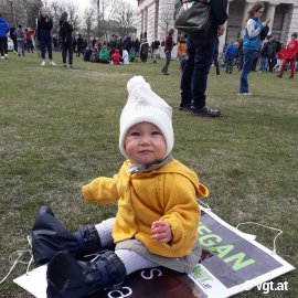 Kond sitzt auf einer Wiese voller Demonstrant_innen