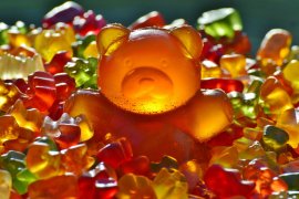 Das Bild zeigt ein riesiges Gummibärchen in Mitten von normalen Gummibärchen.