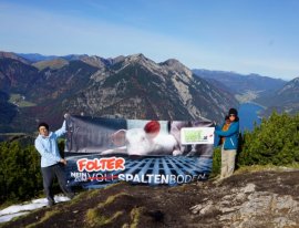 Aktvistinnen halten vor einer eindrucksvolen Bergsee-Kulisse ein Tierschutzbanner in der angenehm wärmenden Sonne.